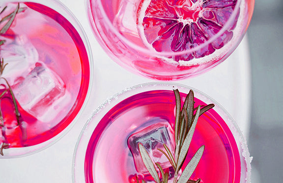 A close up view of a group of three pink cocktails sit on a white platform.